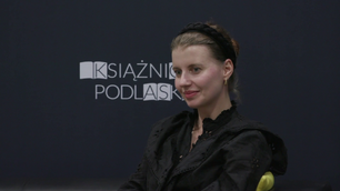 Joanna Glogaza siedzi na tle baneru z logotypem Książnicy Podlaskiej.